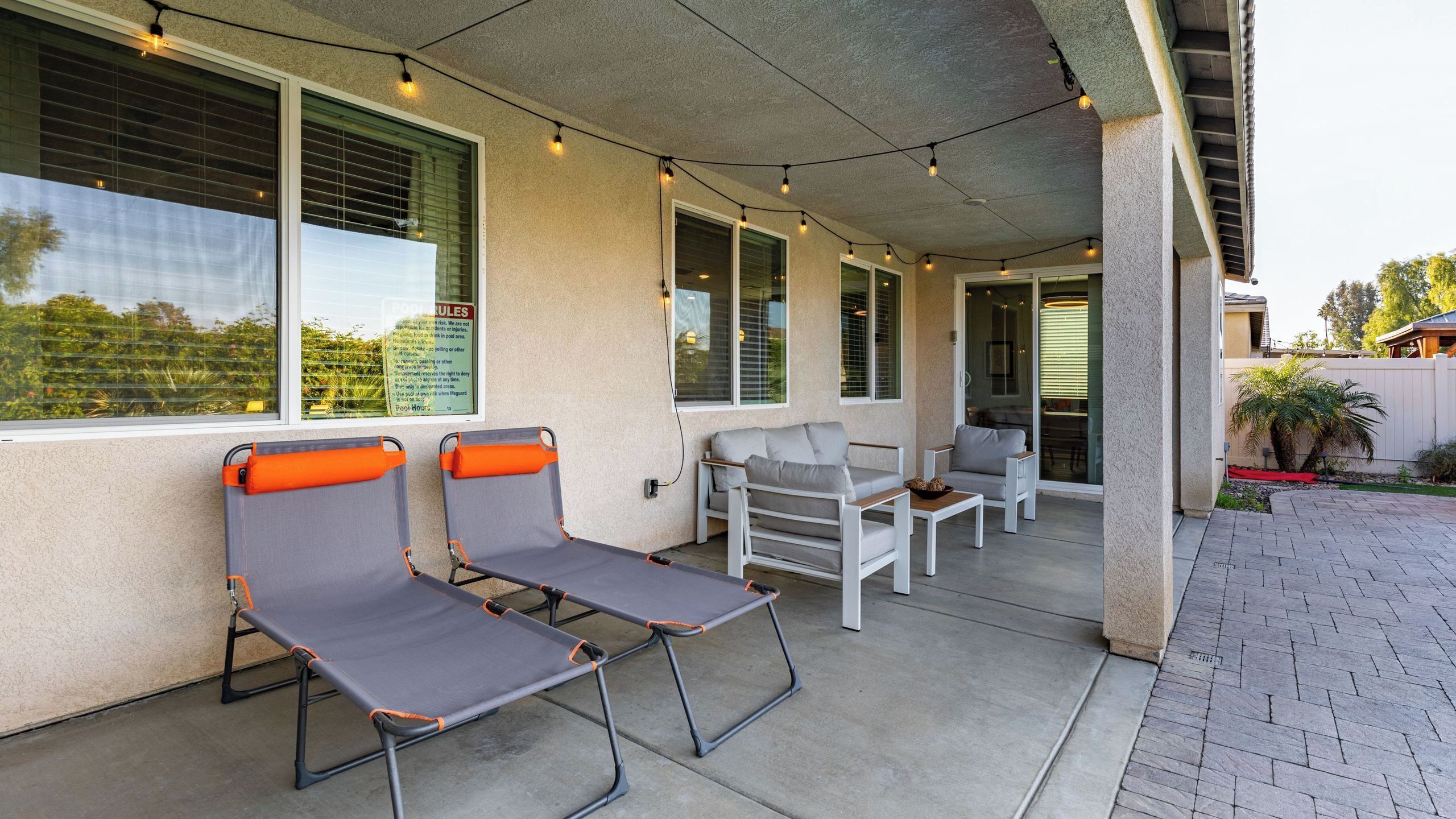 Ein überdachter Patio-Bereich mit zwei Liegestühlen, einem Sofa und einem Esstisch.