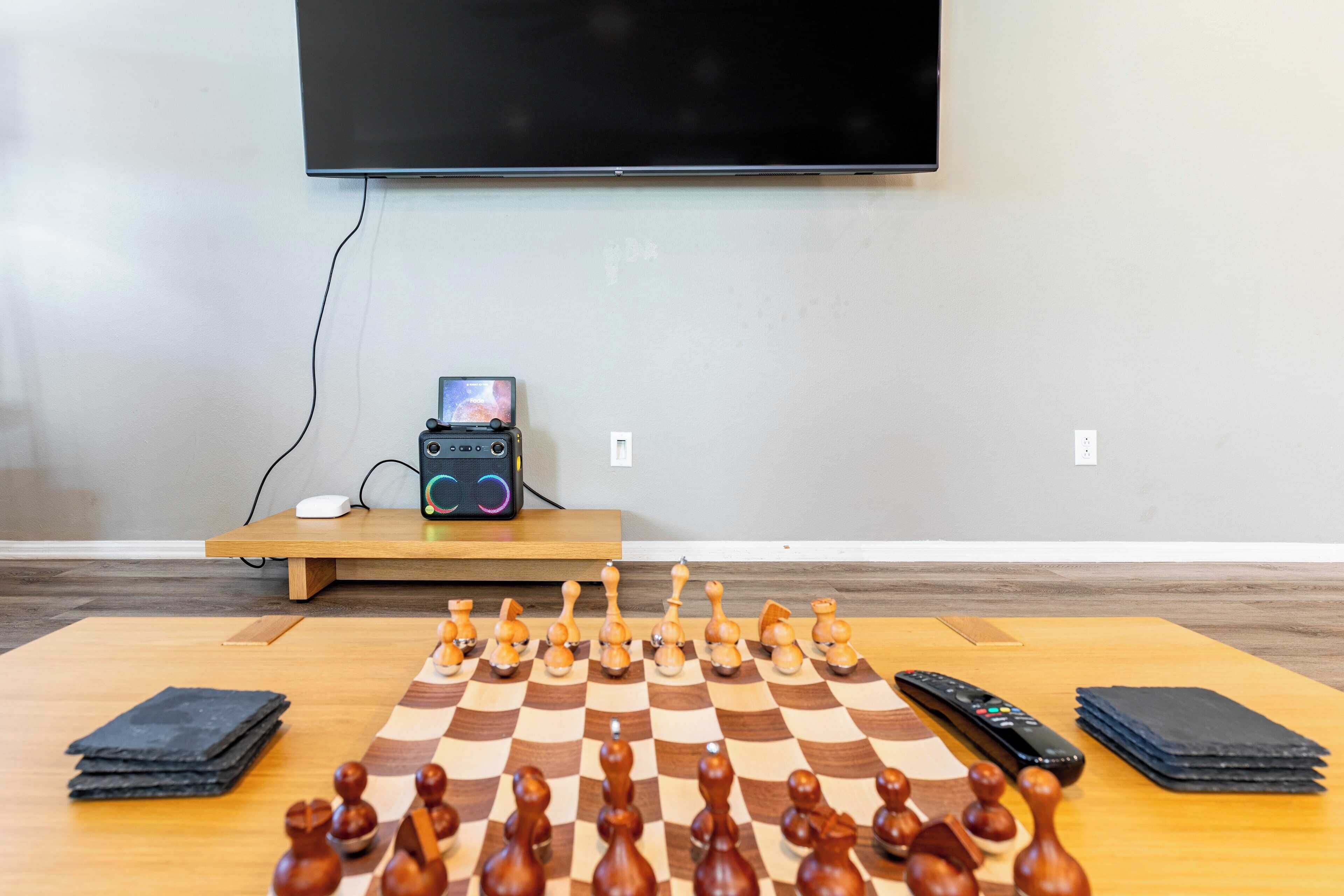 A chessboard set up on a wooden table with a remote control and a smartphone nearby.
