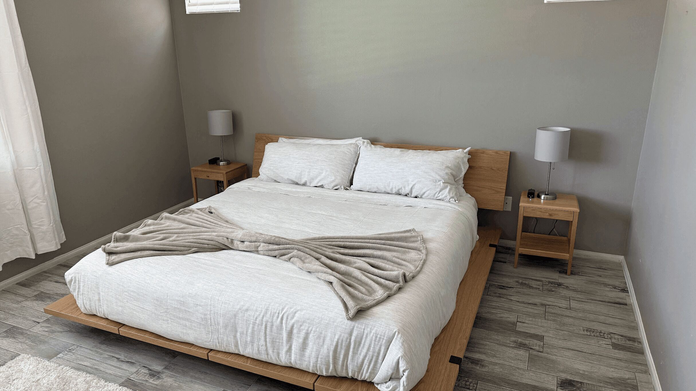 Ein Schlafzimmer mit einem Bett, zwei Nachttischen, einer Lampe auf jedem Tisch und einem Fenster mit Jalousien.