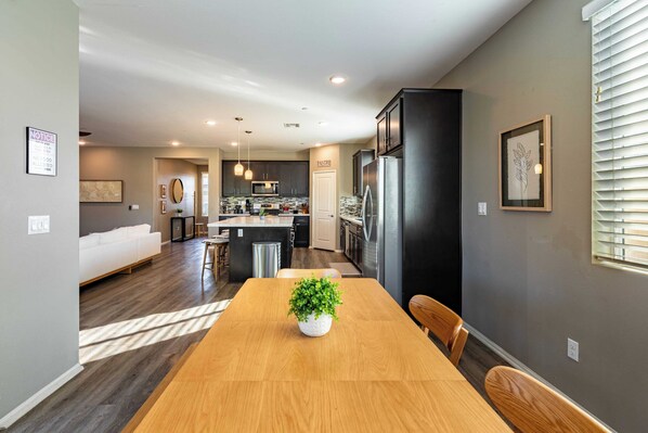 Une cuisine moderne avec des meubles de couleur sombre, un îlot central et un coin repas comprenant une table et des chaises en bois.