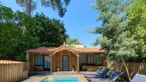 A wooden deck with a rectangular pool, lounge chairs, and a building with a tiled roof.