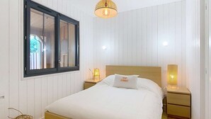 A bedroom with a wooden bed, a window with blinds, a hanging light fixture, and bedside tables with lamps.