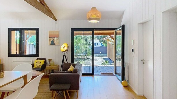 A spacious room with a wooden floor, a dining area with a table and chairs, a sofa, and a large window with a view of the outdoors.