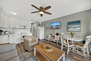 A modern kitchen with white cabinets, a ceiling fan, and a dining area with a wooden table and white chairs.