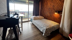 Un dormitorio pequeño con una cama, un escritorio y ventana con vistas a un balcón.