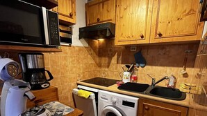 Cocina compacta con armarios de madera, microondas, cafetera, lavadora y pileta.