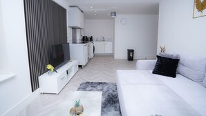 A modern living room with a white sofa, a flat-screen TV, and a kitchen in the background. - Luxury 2 Bedroom Apartment in Birmingham Next to Utility Arena (Birmingham)