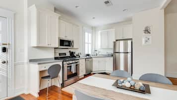 Une cuisine moderne avec des meubles blancs, des appareils en acier inoxydable et un coin repas comprenant une table et des chaises en bois.