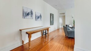 Un salón amplio con suelo de madera, un banco, un sofá gris y tres obras de arte abstracto en la pared.