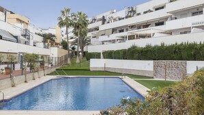 Zona residencial con piscina, edificios de apartamentos blancos y palmeras.