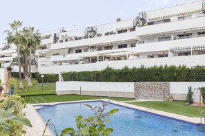 Un hotel moderno con piscina, varios balcones y un jardín bien cuidado.