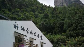 A building with a sign in Chinese characters, surrounded by lush greenery and a prominent rock formation in the background.