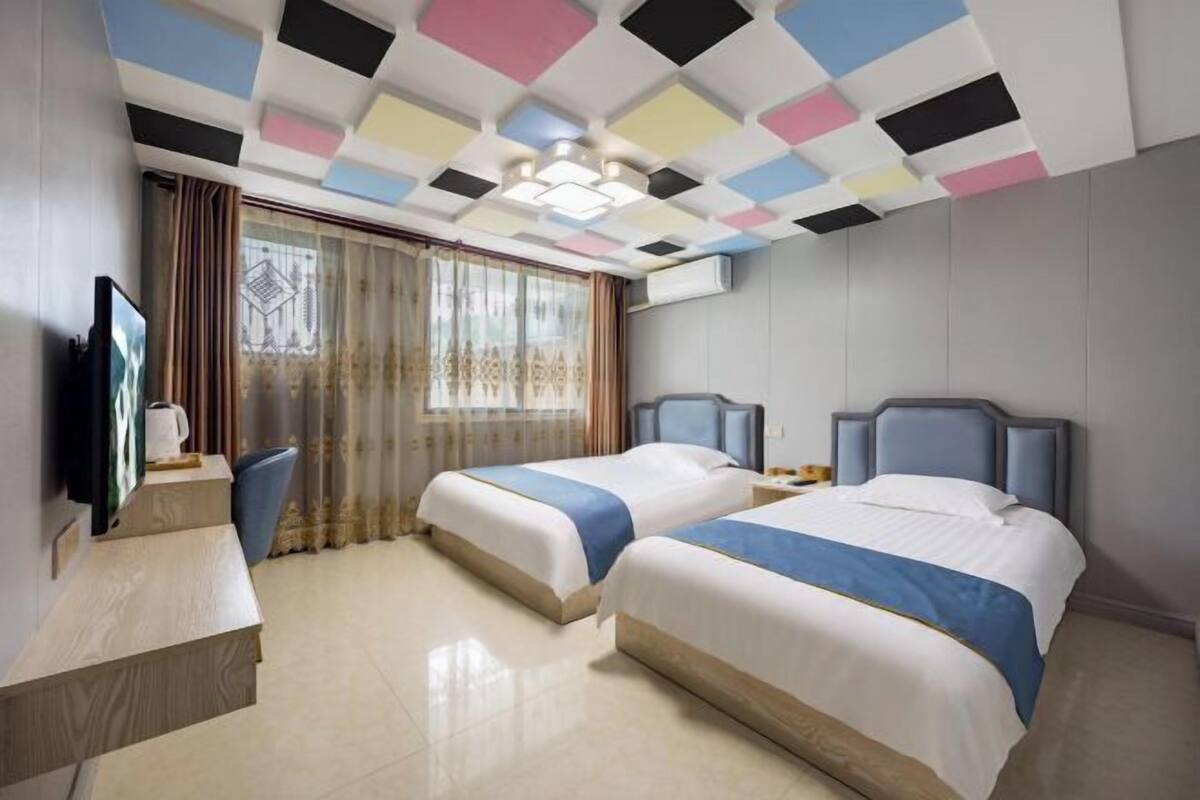 Habitación de hotel con dos camas, un escritorio, un televisor y una ventana con cortinas.