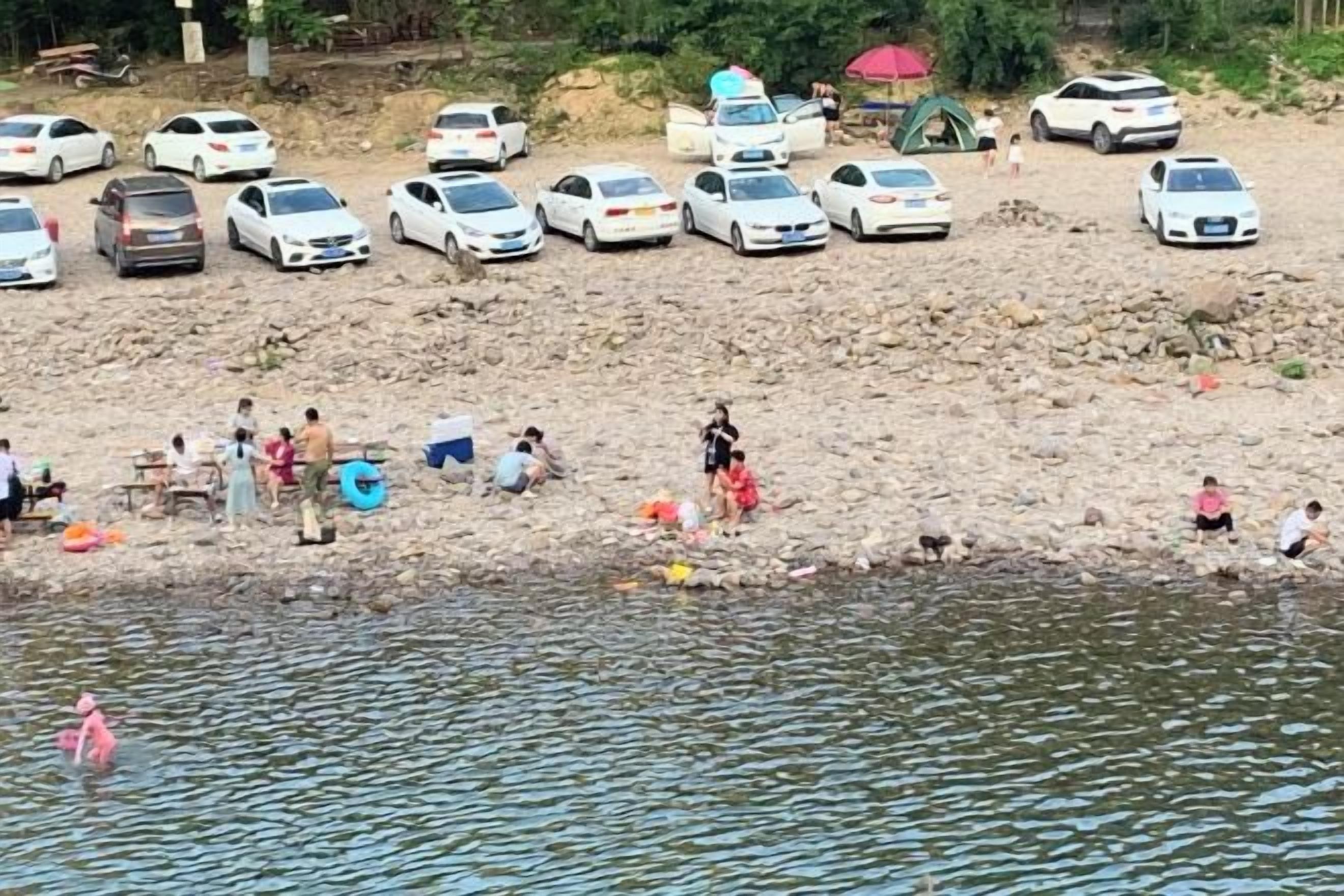 A sandy beach with parked cars and people engaging in various activities near the water.