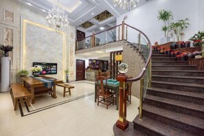 A spacious lobby with a grand staircase, a seating area with a coffee table, and a television. - Old Village Chief Hostel (Xianju)