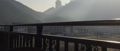 Un balcón con vista a montañas y un edificio lejano.