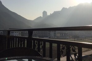 Un balcón con vista a montañas y un edificio lejano.