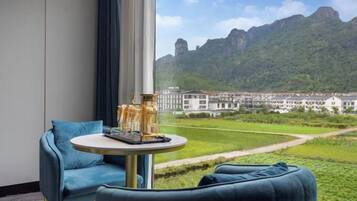 A hotel room with a large window, a round table with a tray, and a view of a mountainous landscape.