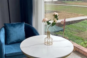 Una habitación con una mesa redonda, un sofá azul y vista a un campo verde por una ventana.