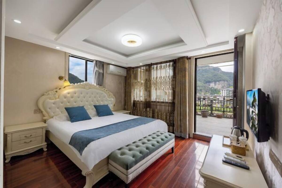 Un dormitorio con una cama grande, una mesita de noche, un banco, un televisor y vistas al exterior.