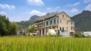A multi-story hotel with a modern design, located in a lush, green area with mountains in the background.