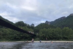 A bridge over water with people on it and a forested hillside in the background. - Old Village Chief Hostel (Xianju)