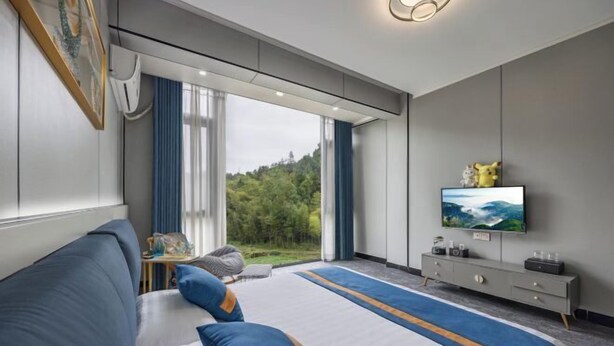 A modern hotel room with a large bed, a TV, a desk, and a view of the outdoors.