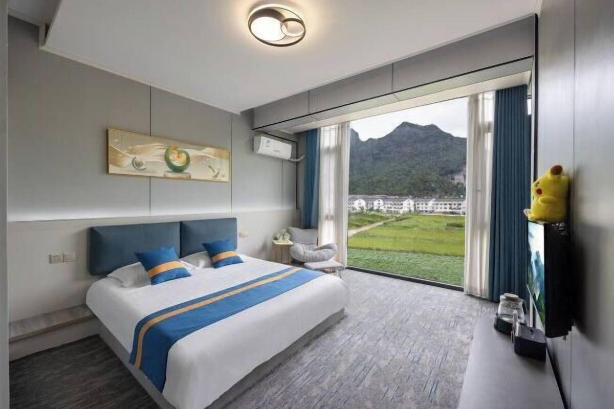 Una habitación de hotel moderna con una cama grande, vistas a una montaña y una ventana con cortinas.