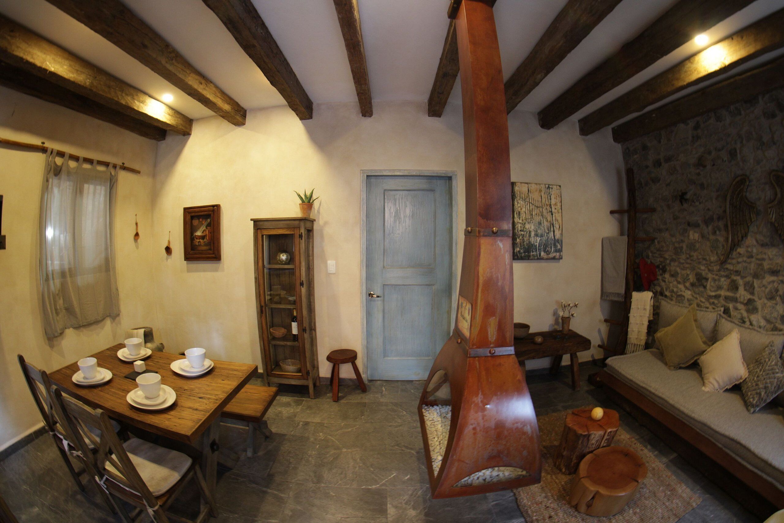 A rustic interior with a wooden dining table, chairs, a stone wall, a wooden bench, and a stone fireplace.