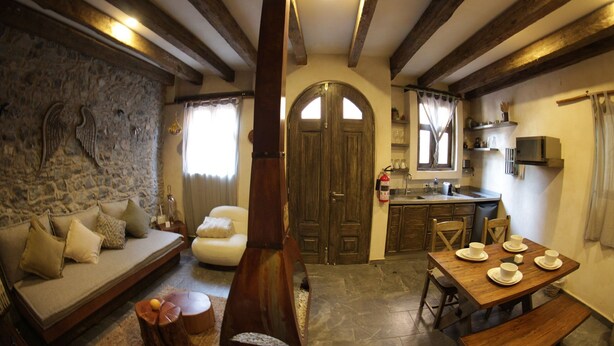 A cozy living room with a stone wall, wooden beams, a sofa, a dining table with plates, and a kitchen area with a microwave. - Vecchia Luna (Val'Quirico)