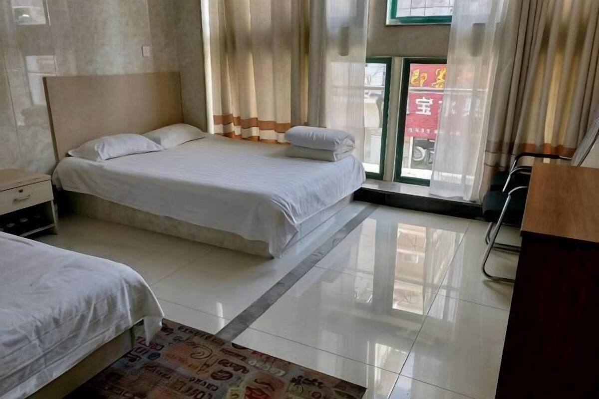 Une chambre d’hôtel avec deux lits, un bureau, une chaise et une fenêtre avec des rideaux.
