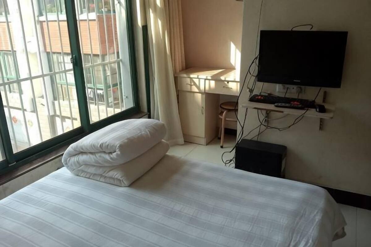 Une chambre d’hôtel avec un lit, un bureau, une télévision et une fenêtre avec des rideaux.