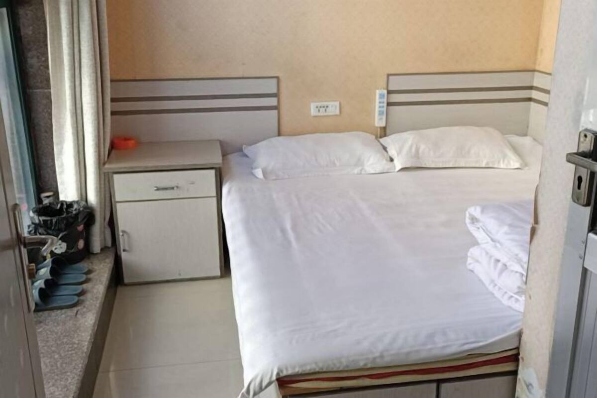 Une petite chambre avec un lit simple, une table de chevet, un tiroir et un petit placard.