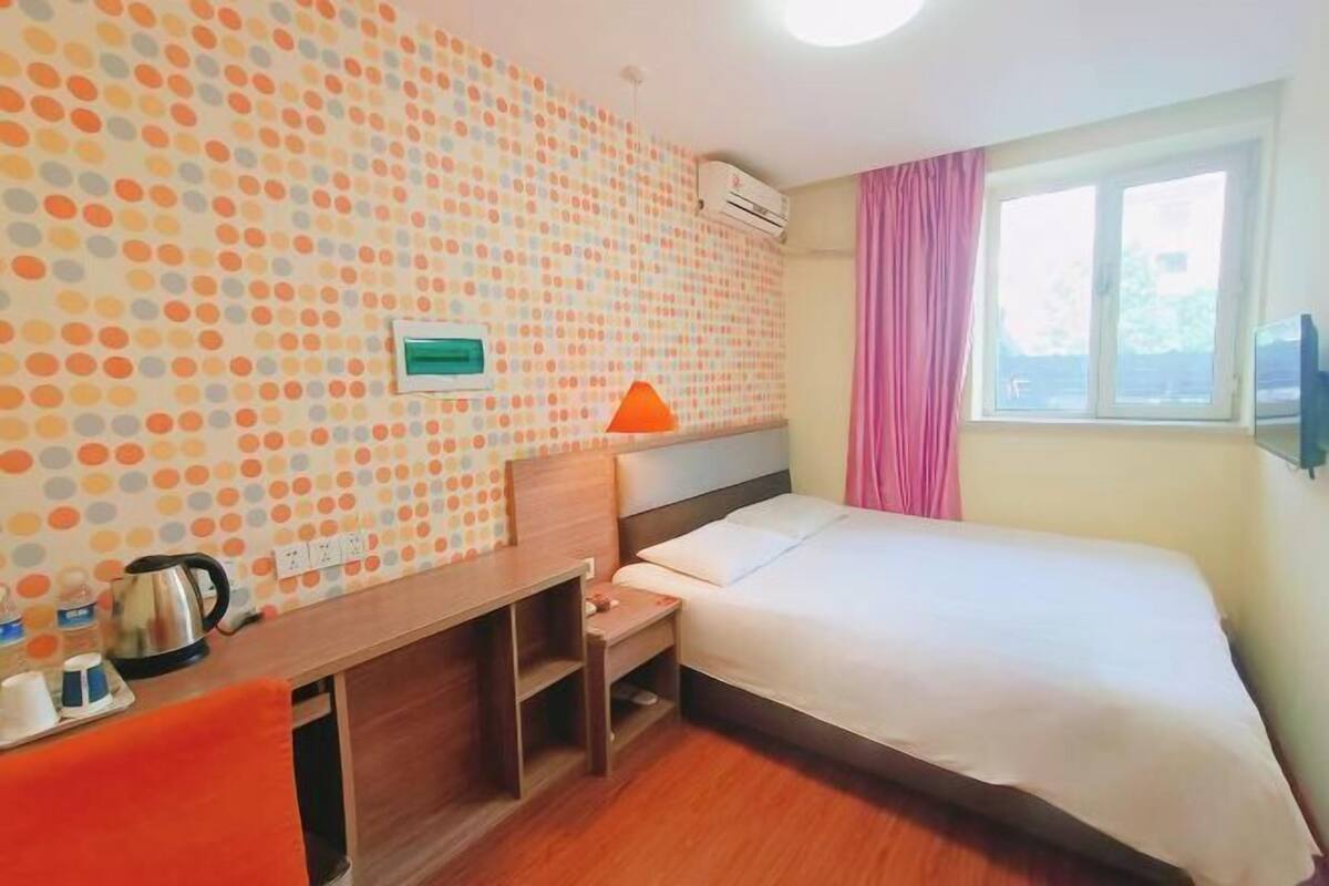 A hotel room with a bed, a desk, a chair, a window with curtains, and a wall with a polka dot pattern.