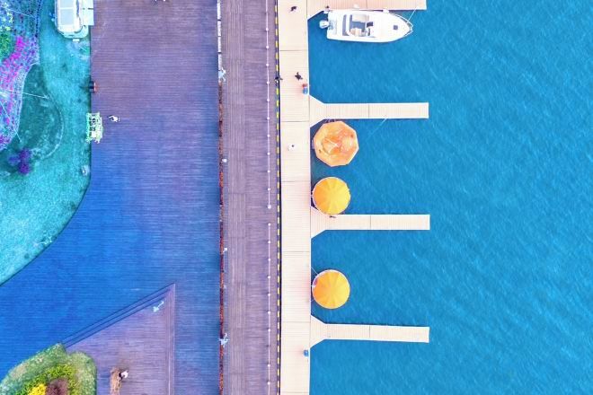 Vista aérea de una propiedad frente al agua, con un muelle, un bote y una fila de sombrillas.