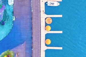 Vista aérea de una propiedad frente al agua, con un muelle, un bote y una fila de sombrillas.