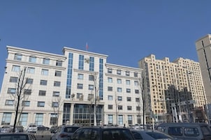 Un edificio de varios pisos con una entrada central, rodeado de automóviles estacionados.