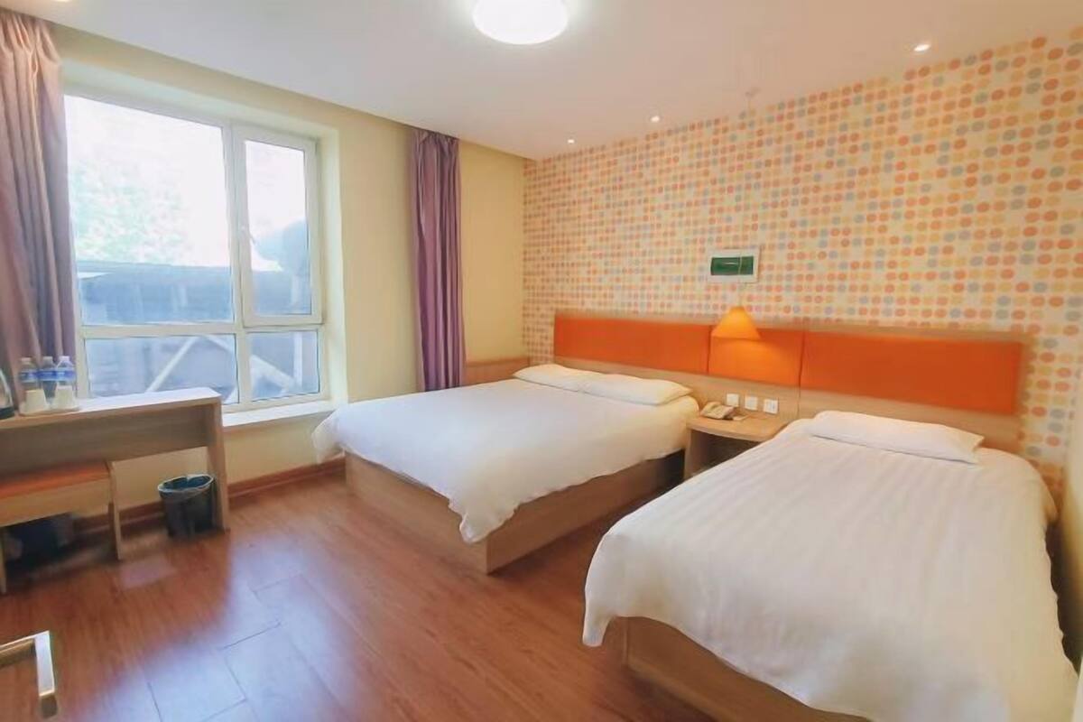 A hotel room with two beds, a desk, a window, and a patterned wall.
