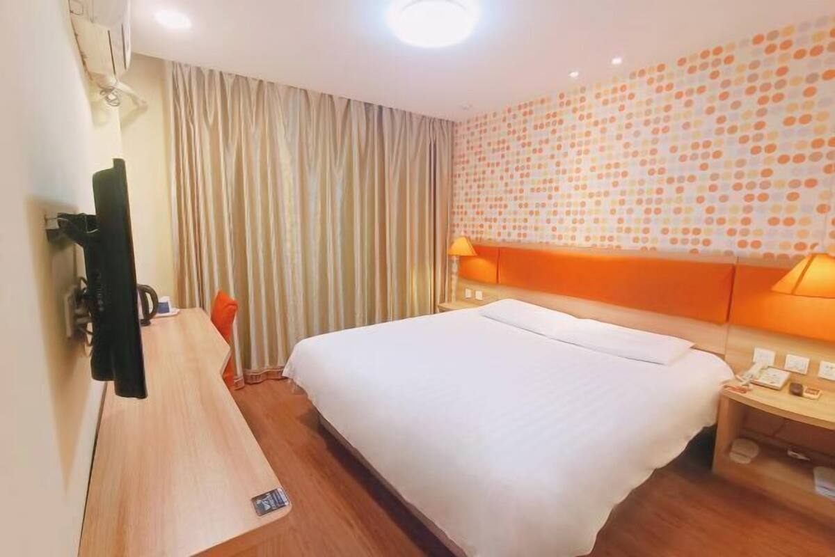 A hotel room with a bed, a desk, a chair, a TV, a lamp, and a wall with a polka dot pattern.