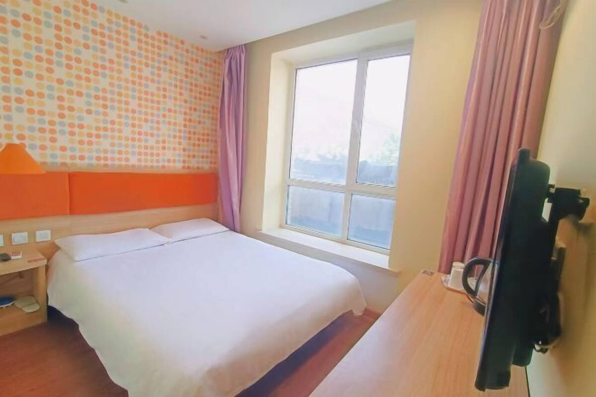 A hotel room with a bed, a window, a television, and a wall with a polka dot pattern.