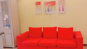 Een rode bank tegen een gele muur, met daarboven drie ingelijste kunstwerken.
