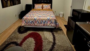 Un dormitorio con una cama, un ventilador de techo, un cuadro en la pared y un microondas.