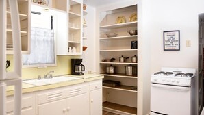 A kitchen with white cabinets, a stove, and shelves with dishes and cookware.