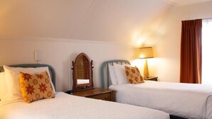 A hotel room with two beds, a nightstand with a lamp, a mirror, and a window with curtains.