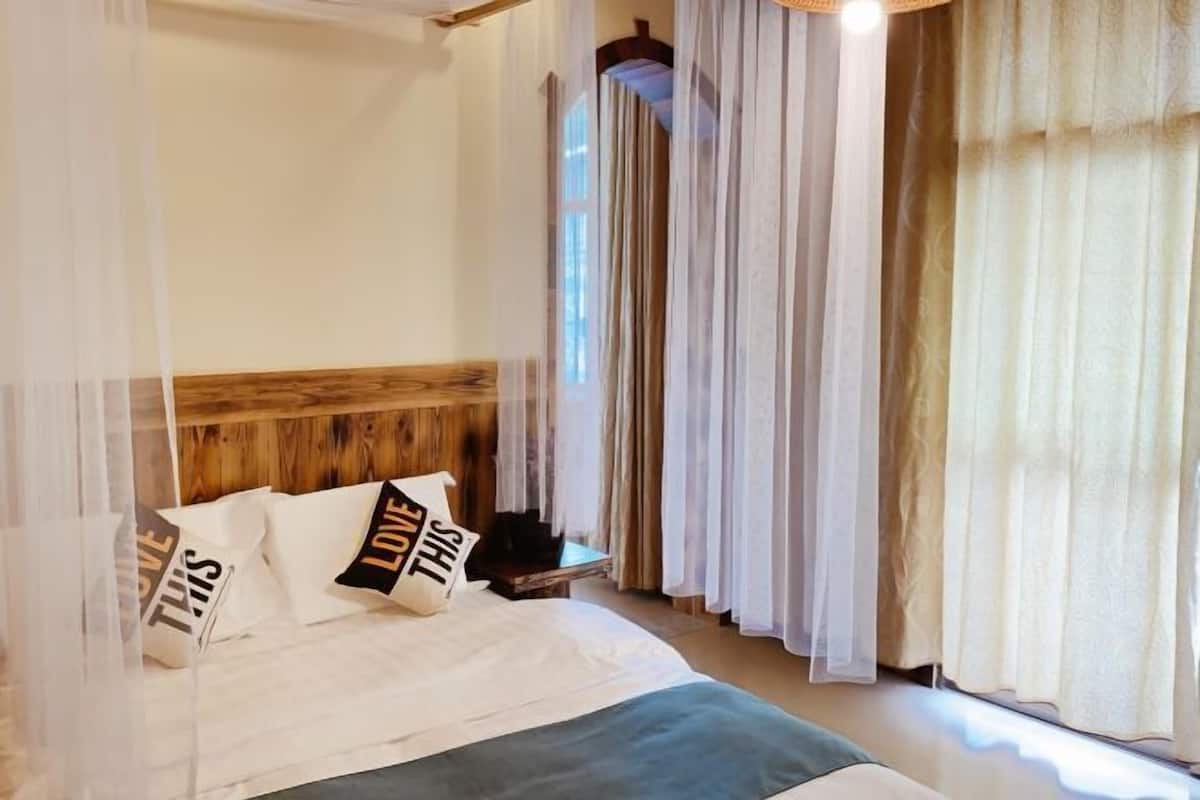 A bedroom with a wooden headboard, a bed with white bedding, and sheer curtains.