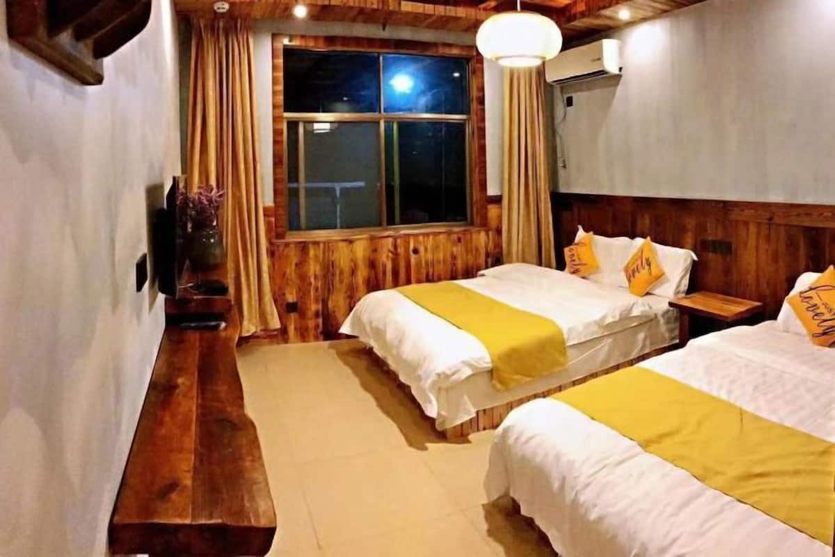 A hotel room with two beds, wooden walls, a large window, and a bench.