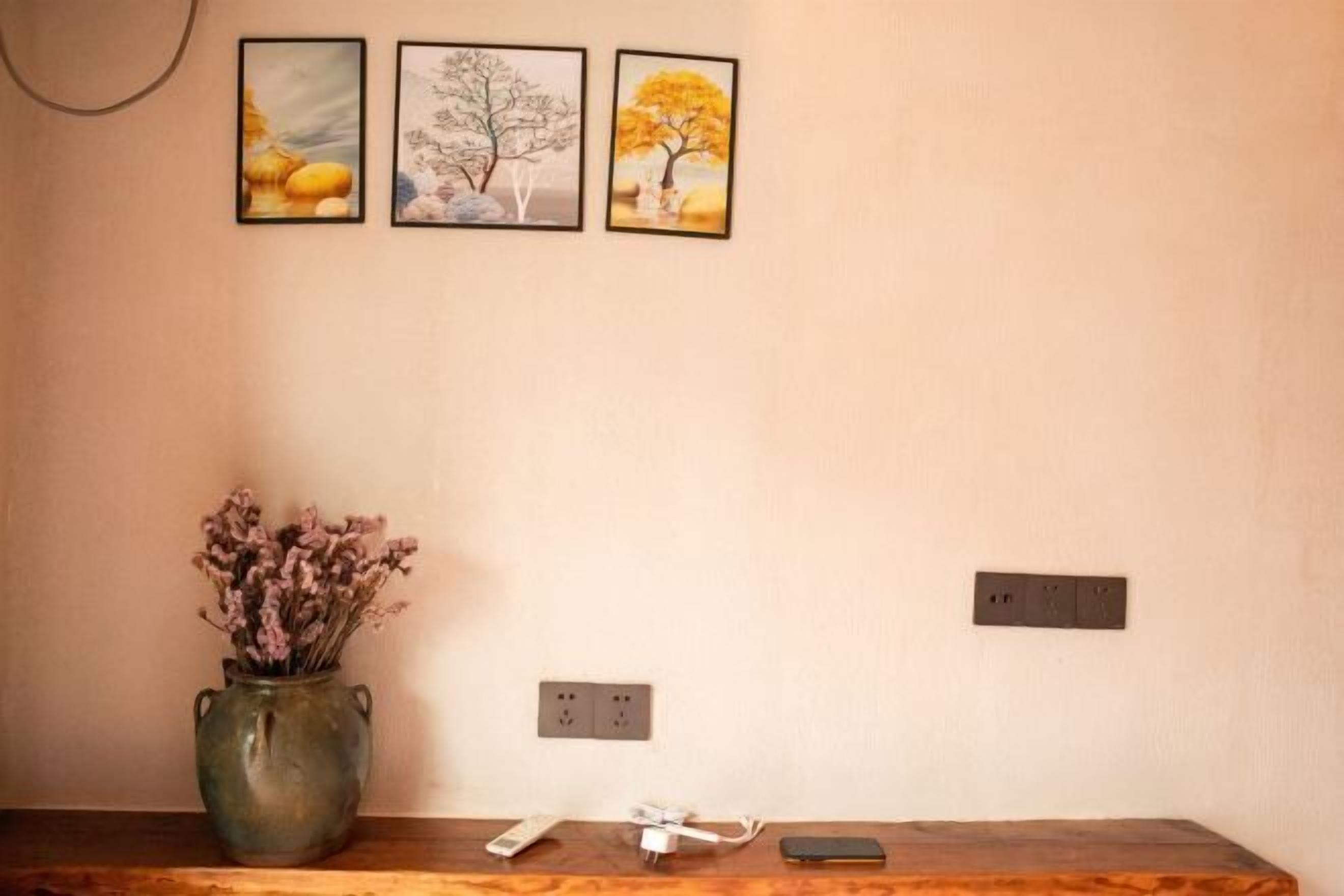 A room with a wooden table, a vase with dried flowers, and three framed pictures on the wall.
