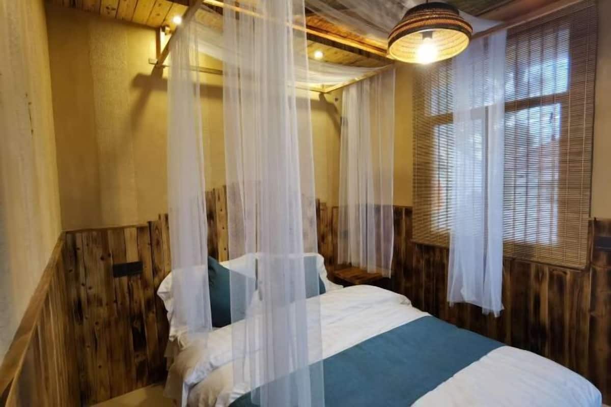A bedroom with a wooden headboard, a bed with white and teal bedding, and sheer curtains.