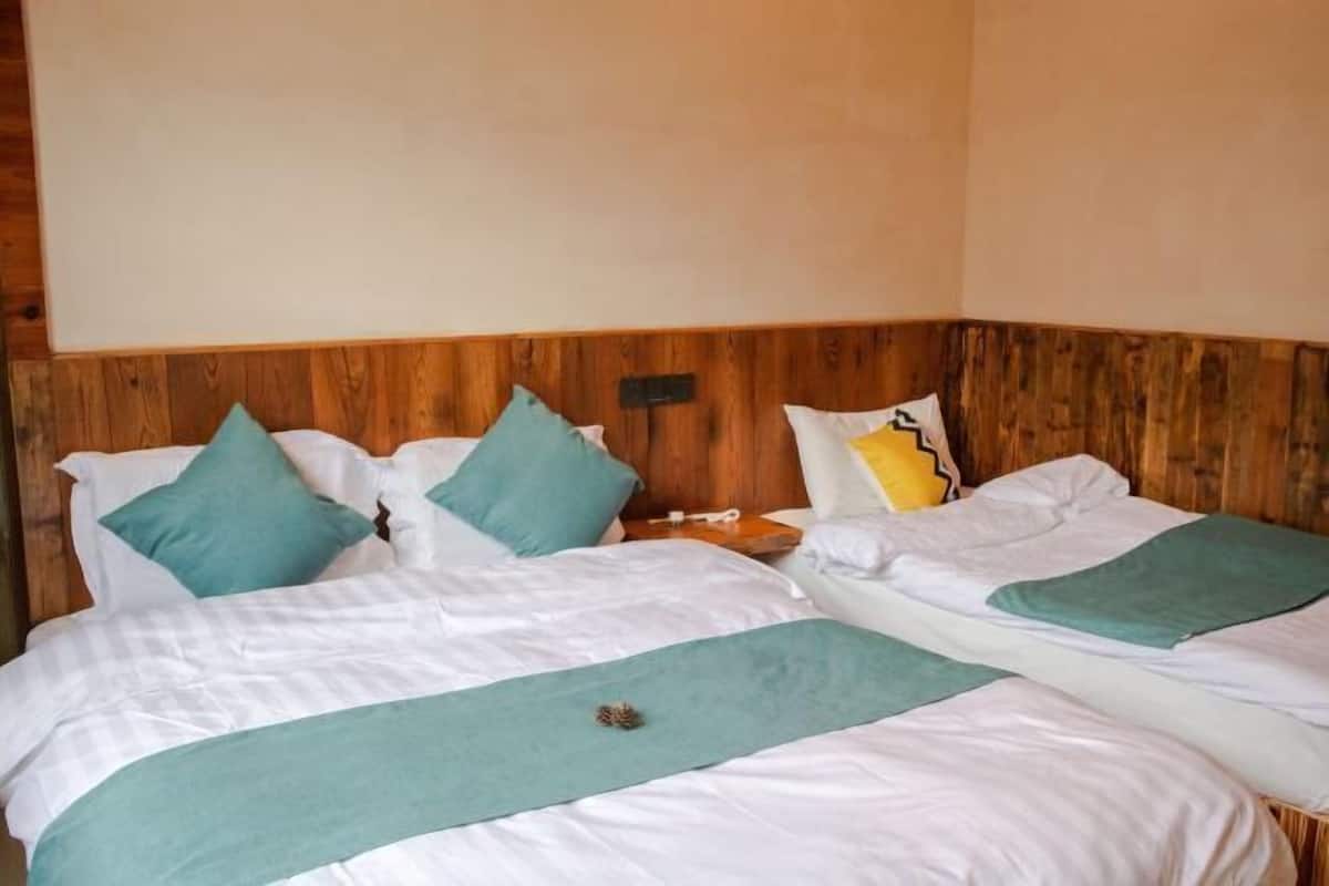 A room with two beds, each with white bedding and teal accents, wooden headboard, and a small nightstand with a lamp.