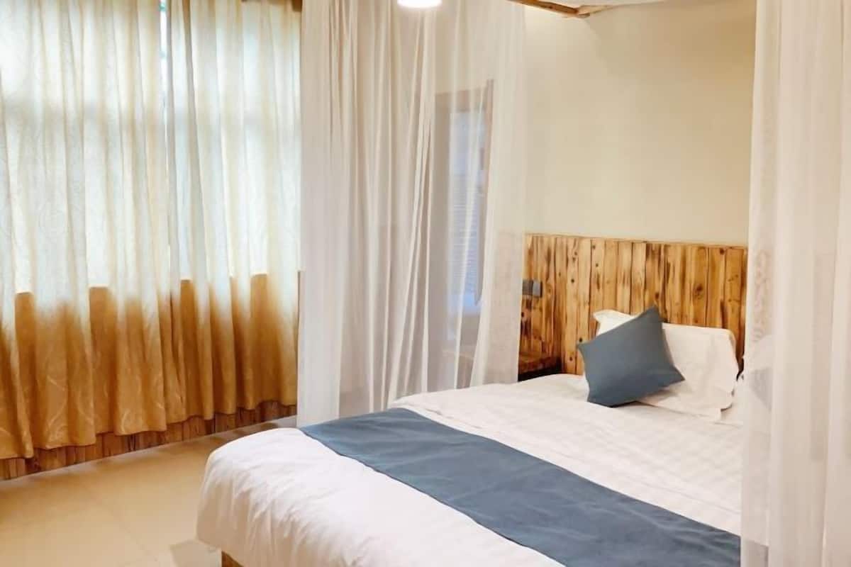 A bedroom with a wooden headboard, a bed with white and blue bedding, and sheer curtains.